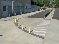 several yellow poles standing in a driveway next to a parking garage on an industrial day