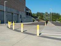 several yellow poles standing in a driveway next to a parking garage on an industrial day