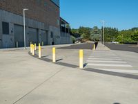 several yellow poles standing in a driveway next to a parking garage on an industrial day