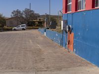 a view of a parking meter on the side of a blue building and a white car parked in front