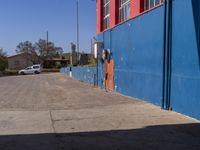 a view of a parking meter on the side of a blue building and a white car parked in front