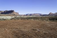 an arid, desert area in front of mountains with sparse bushes and dirt on the ground