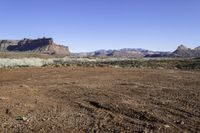 an arid, desert area in front of mountains with sparse bushes and dirt on the ground