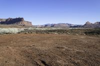 an arid, desert area in front of mountains with sparse bushes and dirt on the ground