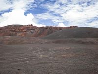 a large hill in an arid area with dirt and small clouds above it by a mountain