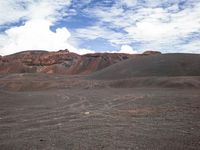 a large hill in an arid area with dirt and small clouds above it by a mountain