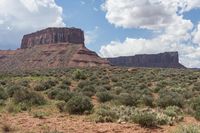 a man rides a horse through an arid landscape with mountains in the background while holding his saddle