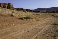 a dirt road leading towards an arid area with mountains in the background and small rocks in front