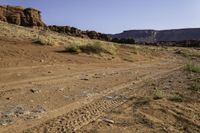 a dirt road leading towards an arid area with mountains in the background and small rocks in front