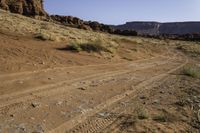 a dirt road leading towards an arid area with mountains in the background and small rocks in front