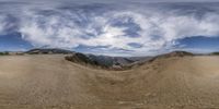 a wide angle view of an arid valley with mountains in the background and clouds in the sky