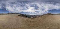 a wide angle view of an arid valley with mountains in the background and clouds in the sky