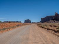 dirt road through arid terrain in deserts with red rocks in background in daylight light, wide angle