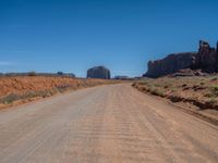 dirt road through arid terrain in deserts with red rocks in background in daylight light, wide angle