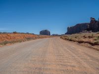 dirt road through arid terrain in deserts with red rocks in background in daylight light, wide angle