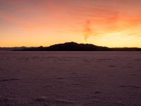 an orange sunset over the mountains and snow covered field at sunrise in winter time in arizona