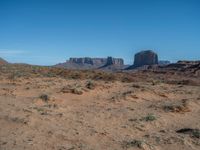 the rocks and dirt of monument valley are in view against a blue sky and mountains