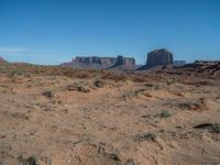 the rocks and dirt of monument valley are in view against a blue sky and mountains