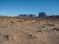 the rocks and dirt of monument valley are in view against a blue sky and mountains