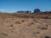 the rocks and dirt of monument valley are in view against a blue sky and mountains