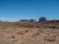 the rocks and dirt of monument valley are in view against a blue sky and mountains