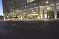 the entrance to a large, glassed building at night with a parking meter visible