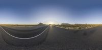 a desert road is shown through a fish eye lens as the sun rises behind a hill