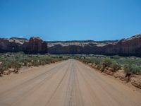 a large dirt road near the edge of a desert with a mountain in the background