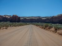 a large dirt road near the edge of a desert with a mountain in the background