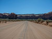 a large dirt road near the edge of a desert with a mountain in the background