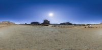 a panorama panoramic photograph of the desert, and sand, with an old car and buildings in the distance