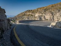 a wide mountain road near the cliff side, with a light blue sky and some rocks