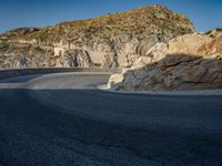 a wide mountain road near the cliff side, with a light blue sky and some rocks