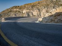 a wide mountain road near the cliff side, with a light blue sky and some rocks