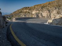 a wide mountain road near the cliff side, with a light blue sky and some rocks