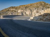 a wide mountain road near the cliff side, with a light blue sky and some rocks