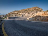 a wide mountain road near the cliff side, with a light blue sky and some rocks