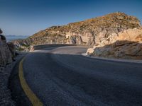 a wide mountain road near the cliff side, with a light blue sky and some rocks