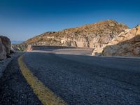 a wide mountain road near the cliff side, with a light blue sky and some rocks