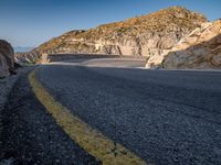 a wide mountain road near the cliff side, with a light blue sky and some rocks