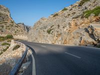 a curved road between large rocky mountains with small green trees on each side of the road