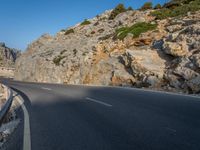 a curved road between large rocky mountains with small green trees on each side of the road