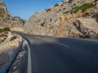 a curved road between large rocky mountains with small green trees on each side of the road