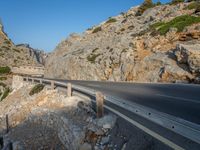 a curved road between large rocky mountains with small green trees on each side of the road