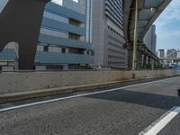 the motorcycle is driving down the road near the city buildings and blue sky with clouds in the background