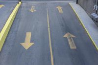 arrow symbols painted on a roadway with a light pole in the distance and a street lined by yellow curbing