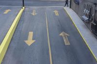 arrow symbols painted on a roadway with a light pole in the distance and a street lined by yellow curbing