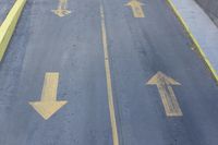 arrow symbols painted on a roadway with a light pole in the distance and a street lined by yellow curbing