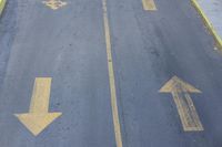 arrow symbols painted on a roadway with a light pole in the distance and a street lined by yellow curbing