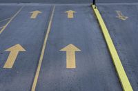 arrow symbols painted on a roadway with a light pole in the distance and a street lined by yellow curbing